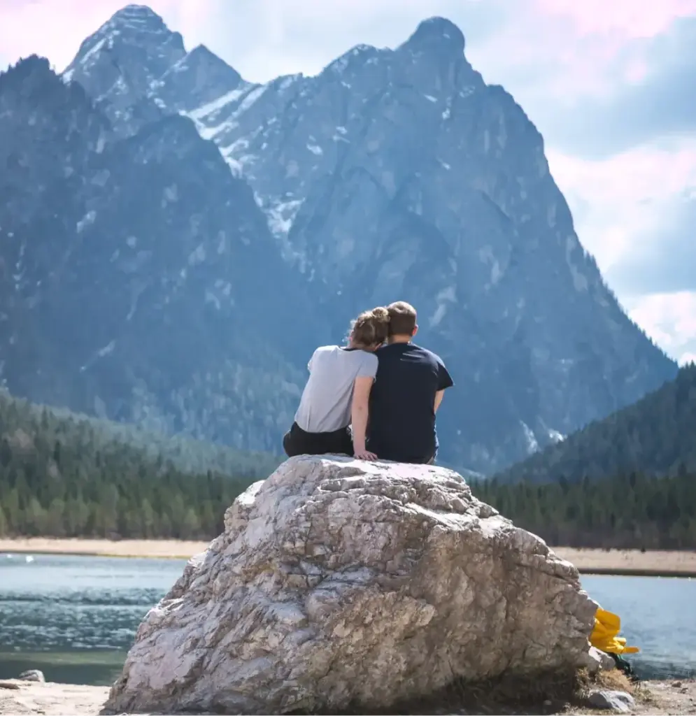 Paar sitzt auf einem Felsen und schaut auf einen Bergsee